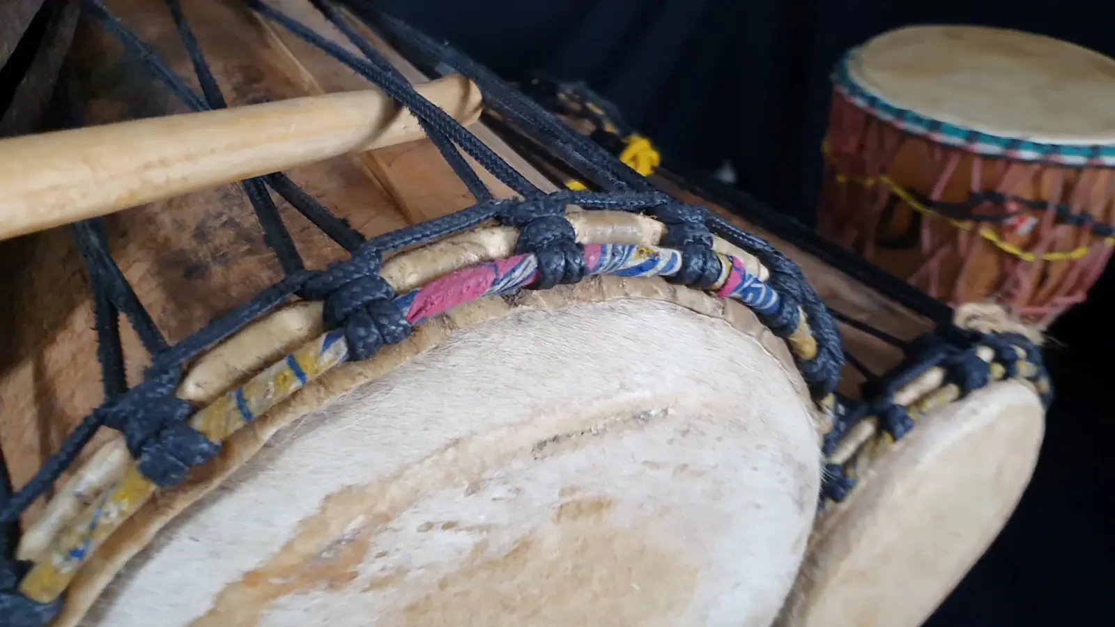 An atabaque drumhead with a drumstick resting on the skin, in warm light.